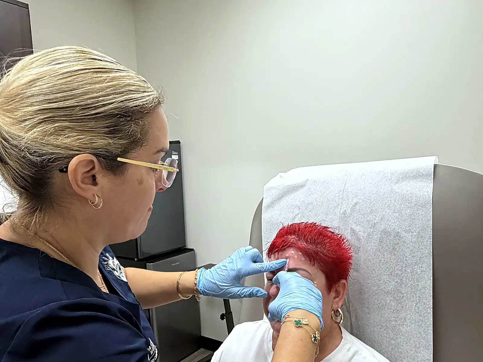 A PassQual Health clinician in gloves performing a facial aesthetic treatment on a seated patient