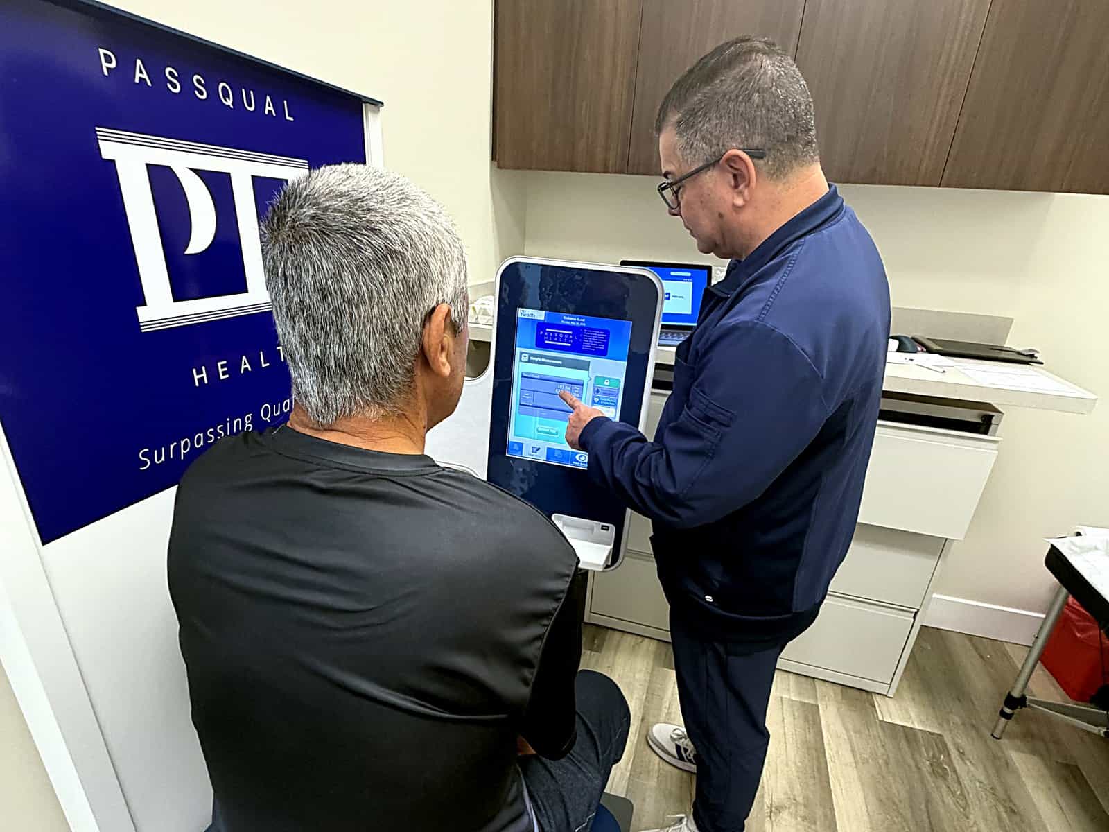 A patient using a PassQual Health self-check-in kiosk with a staff member’s assistance before an appointment