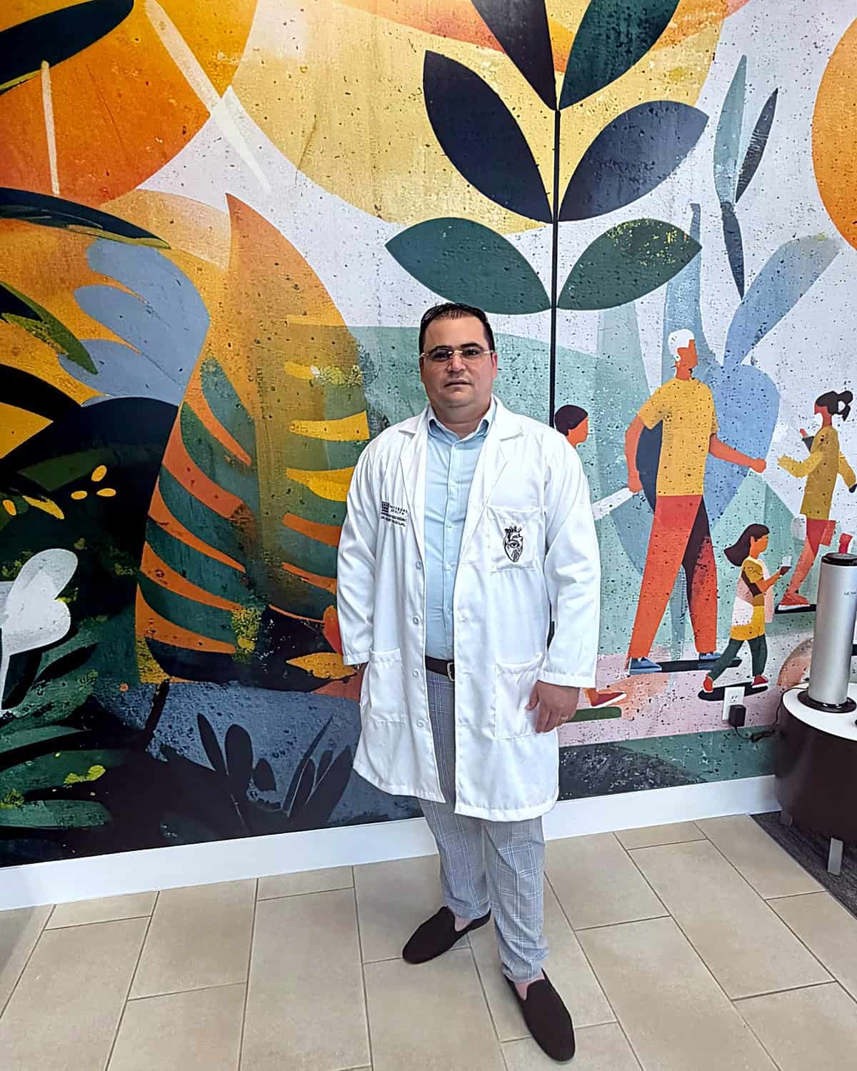 Dr. Hendry Pascual in front of the community wellness mural at PassQual Health